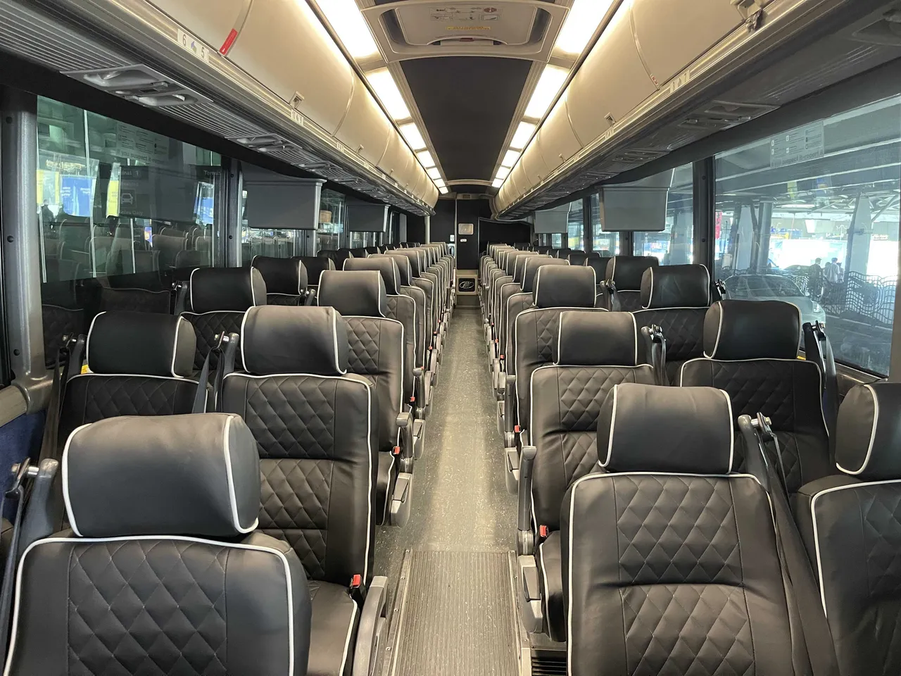 56 Passenger Motorcoach interior with TV screens and overhead parcel racks for charter bus rental