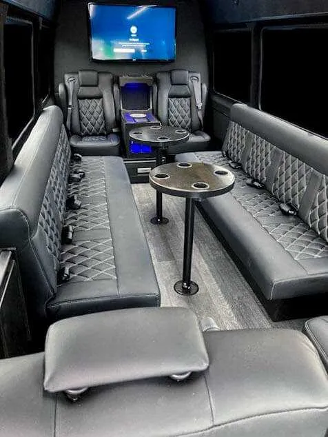 Inside of the 12 Passenger Sprinter Van, showing perimeter lounge seating, captain's chairs and passenger tables, shot 2
