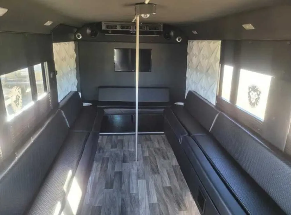 Tuxedo Party Bus interior with perimeter lounge seating, wood-look flooring and TV screens for party bus rental in Schertz, TX
